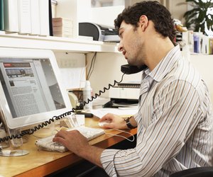 Male office worker balancing phone on shoulder, looking at computer