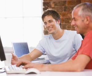 Two businessmen in office typing on computer and s