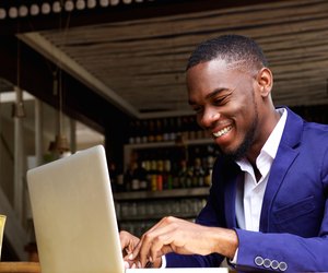 Smiling african businessman working on laptop at cafe