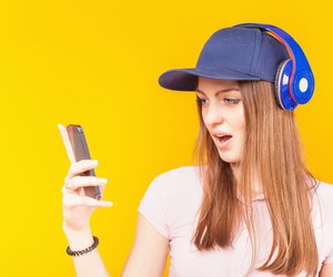 Surprised teenage girl uses a headphones and mobile phone