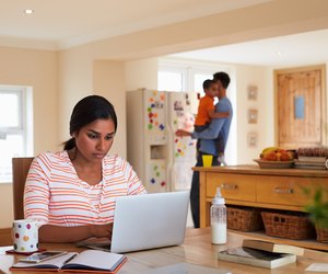 Family In Kitchen With Mother Using Laptop At Table