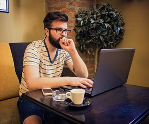 Cheerful Young Man Using Laptop In Coffee Shop