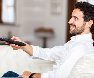 Man on the couch switches remote control TV channels