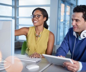 Two colleages discussing ideas using a tablet and computer