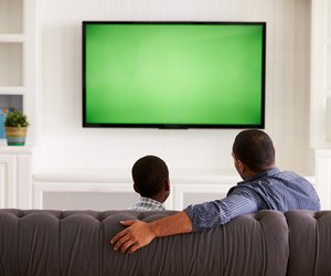 Father and son watching TV at home together, back view