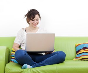 Full length of happy young woman using laptop while sitting on green sofa