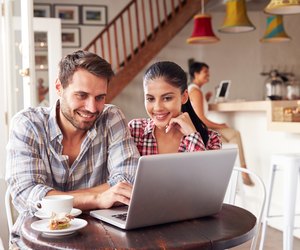 Young couple using laptop in a cafe smiling