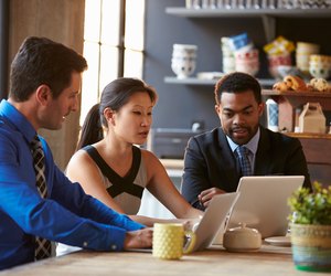 Three Businesspeople Working At Laptop In cafe
