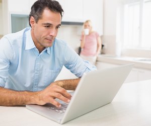 Man using laptop with woman drinking coffee at kitchen