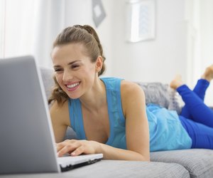 happy young woman laying on divan and using laptop