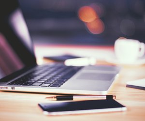 Opened laptop with smartphone, pen and cup of coffee