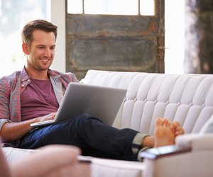 Man Relaxing On Sofa At Home Using Laptop Computer