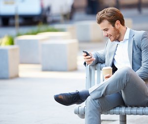 Businessman On Park Bench With Coffee Using Mobile Phone