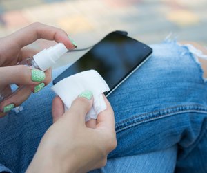 Female hand holding spray and cloth for cleaning the phone