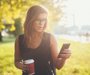 Beautiful young woman holding phone and coffee to go