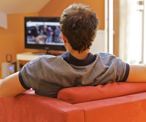 Rear view of a young man watching tv on a red chair