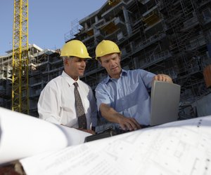 Two Men Wearing Hard Hats Looking Down at a Laptop Computer on a Building Site
