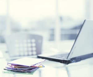 Laptop on desk with pile of CD cases on desk, close up