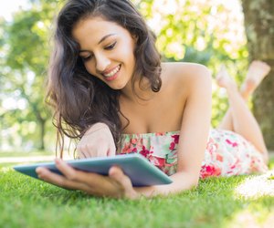 Stylish cheerful brunette lying on a lawn using tablet