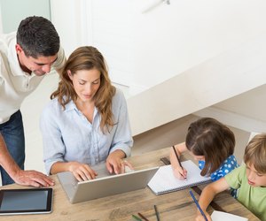 Parents using laptop while children coloring at home