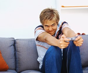 Front view of young man sitting on sofa and playing computer game