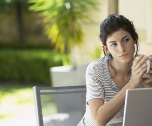 Young woman with mug thinking by laptop