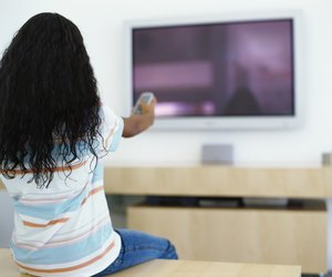 rear view of a girl pointing a remote to a television