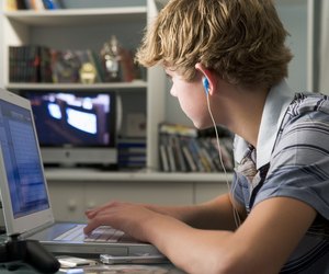 Young boy in bedroom using laptop and listening to