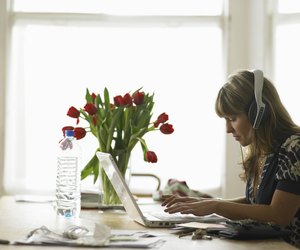 Young woman wearing headphones using laptop on dining table