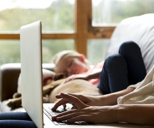 Mother using laptop whilst daughter sleeps