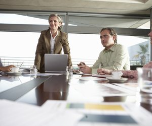 Mature woman standing in business meeting with seated colleagues