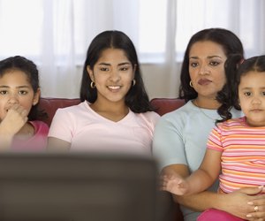 Mid adult woman watching television with her three daughters