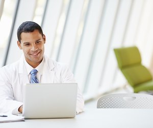 Doctor Using Laptop Sitting At Desk In Modern Hospital