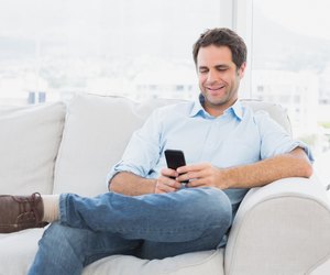 Cheerful man sitting on the couch using his smartphone