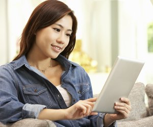 Young Chinese Woman Using Digital Tablet Whilst Relaxing On Sofa