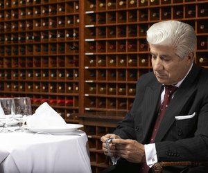Senior man sitting at table in restaurant looking at watch