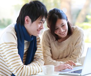 Man and woman sat smiling at laptop with cup and saucer