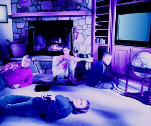 Wired family looking at viewer Father at laptop, mother holding phone, son in front of video game, daughter wearing headset