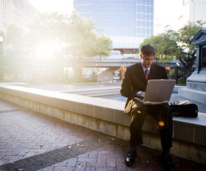 Businessman using laptop computer by sidewalk