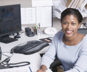 Woman sitting at desk in office, smiling, portrait
