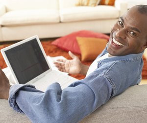 Mature man on sofa with laptop, smiling, portrait