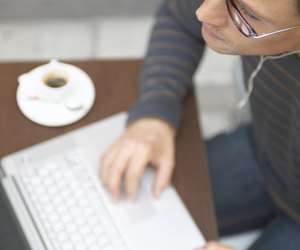 "Man sitting at cafe table using laptop computer, close-up"