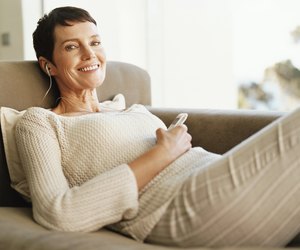 Mature Woman Lies on a Chaise-Lounge Wearing an Earpiece and Holding a Mobile Phone