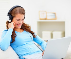 Cute young female listening to music on the laptop
