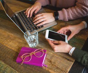 Hands over laptop and smartphone on wooden table with glasses