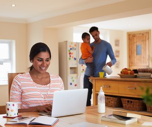 Family In Kitchen With Mother Using Laptop At Table