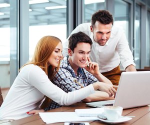 Smiling students sitting in a canteen with a laptop