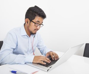 Young businessman listening music while using laptop in office
