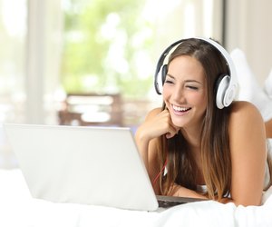 Girl with headphones reading in a laptop at home