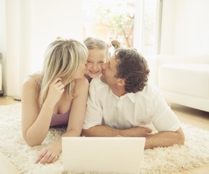 Mother and father kissing girl on rug